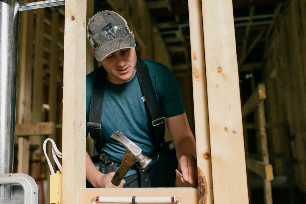 safety glasses, hammer, wood, framing, construction, green t-shirt, ball cap